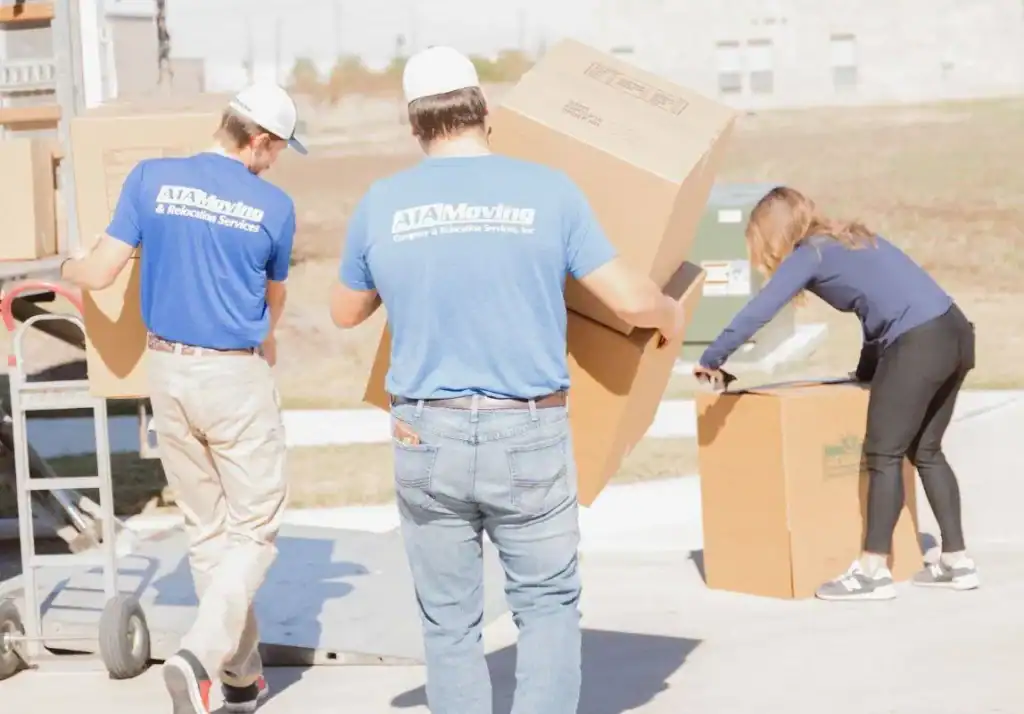 A1A movers carrying a large box past a customer packing in the driveway