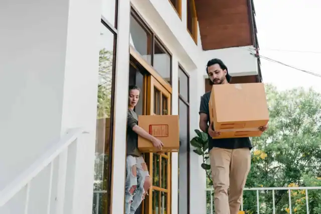 Couple carrying moving boxes at the front door of a house