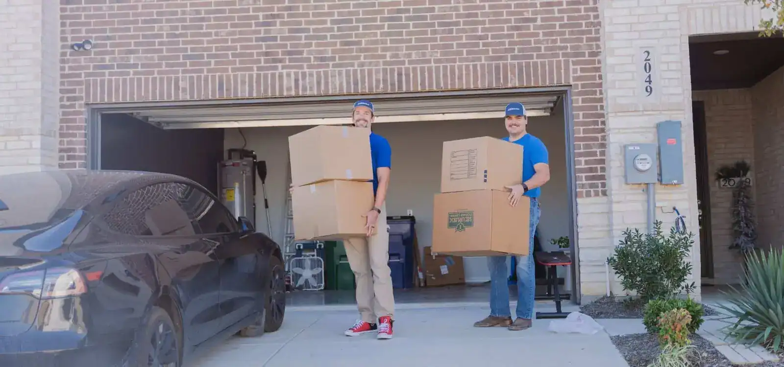 Two A1A movers carrying stacked boxes out of a garage
