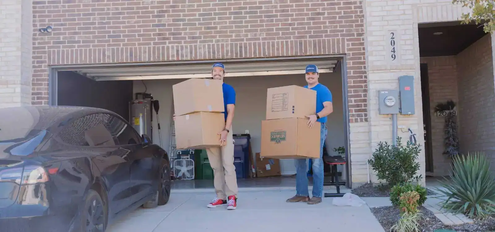 Two A1A movers carrying stacked boxes out of a garage
