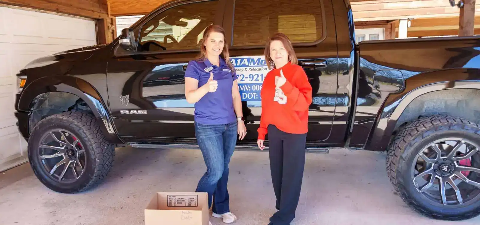 Two women giving a thumbs up next to a pickup truck in a garage
